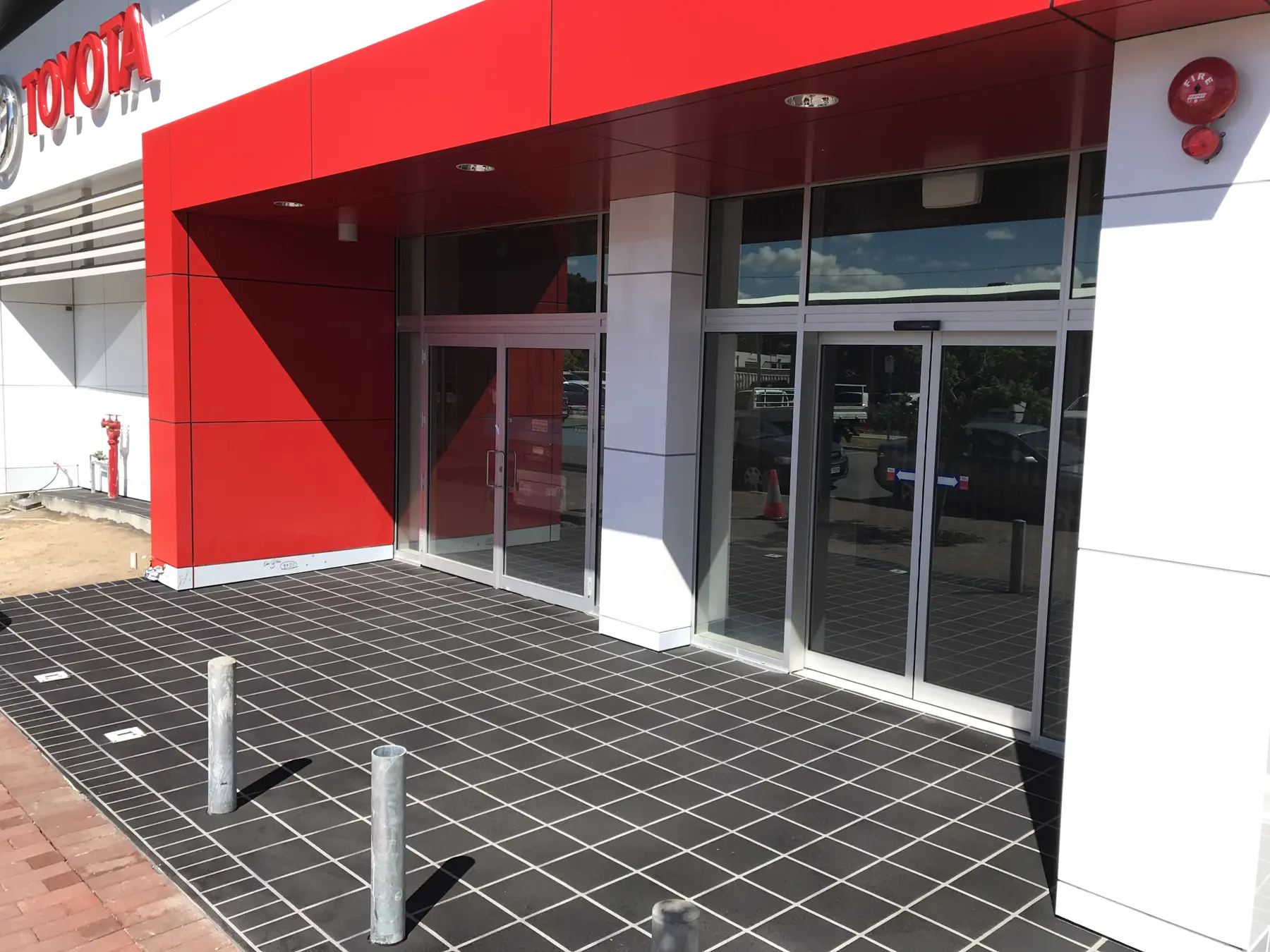 Charcoal stencil concrete forecourt in a square tile pattern with white joint lines at a car dealership entry