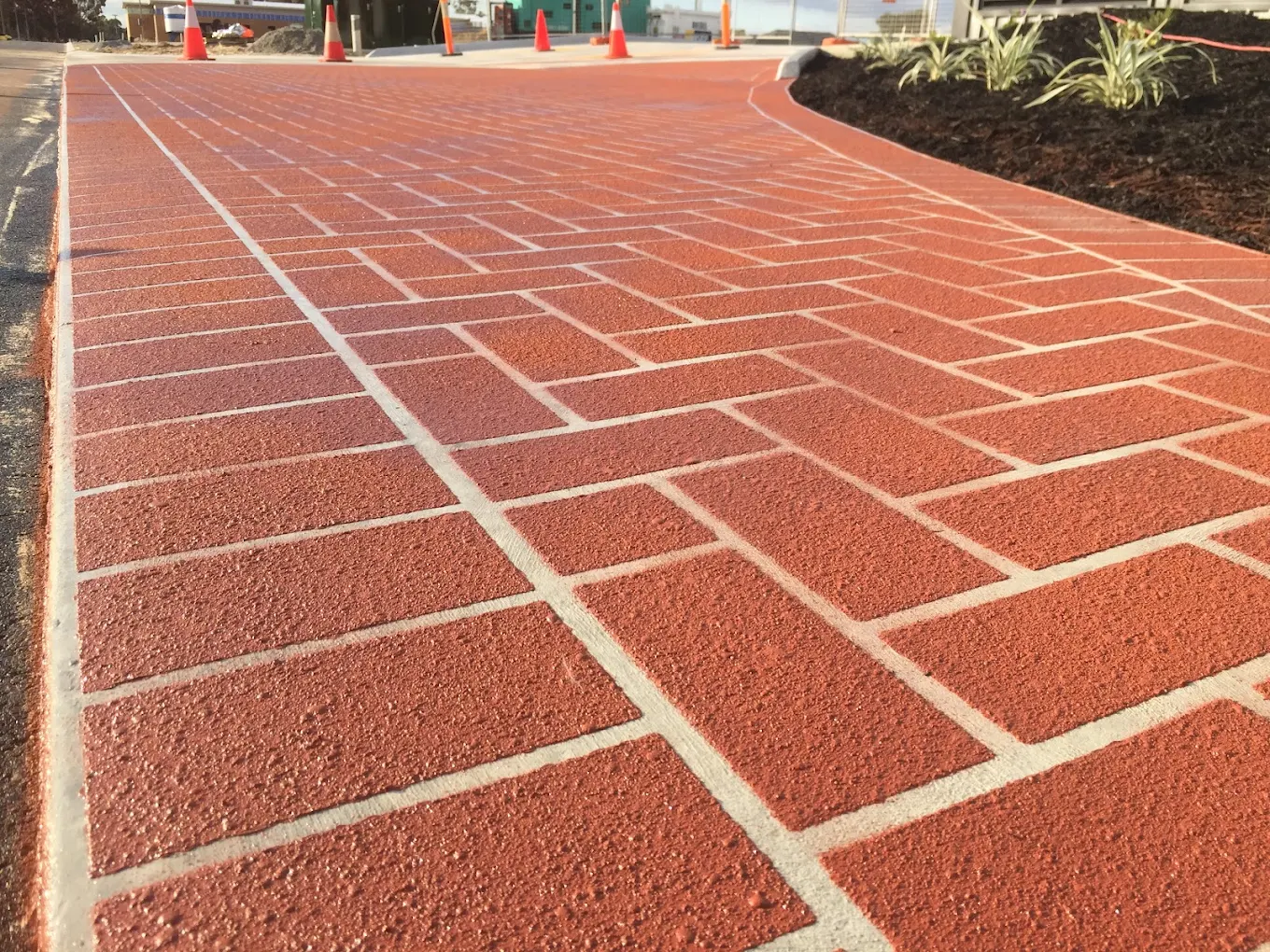 Red brick-pattern spray-on paving across a wide commercial apron with traffic cones in place