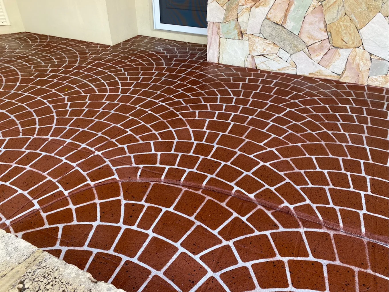 Terracotta spray-on paving in a European fan cobble pattern wrapping around a stone-clad entry