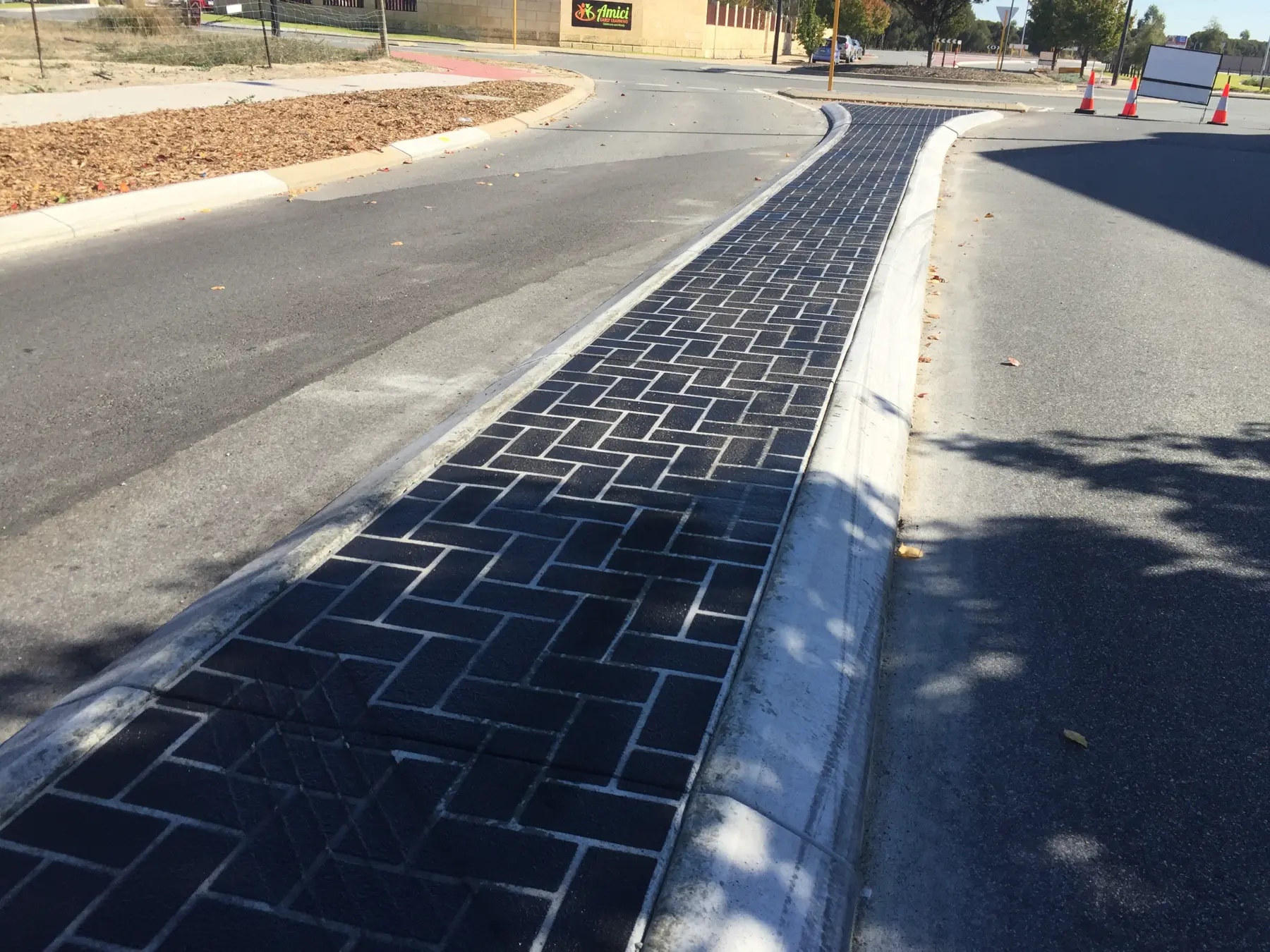 Black brick-pattern stencil concrete median curving alongside a kerb line