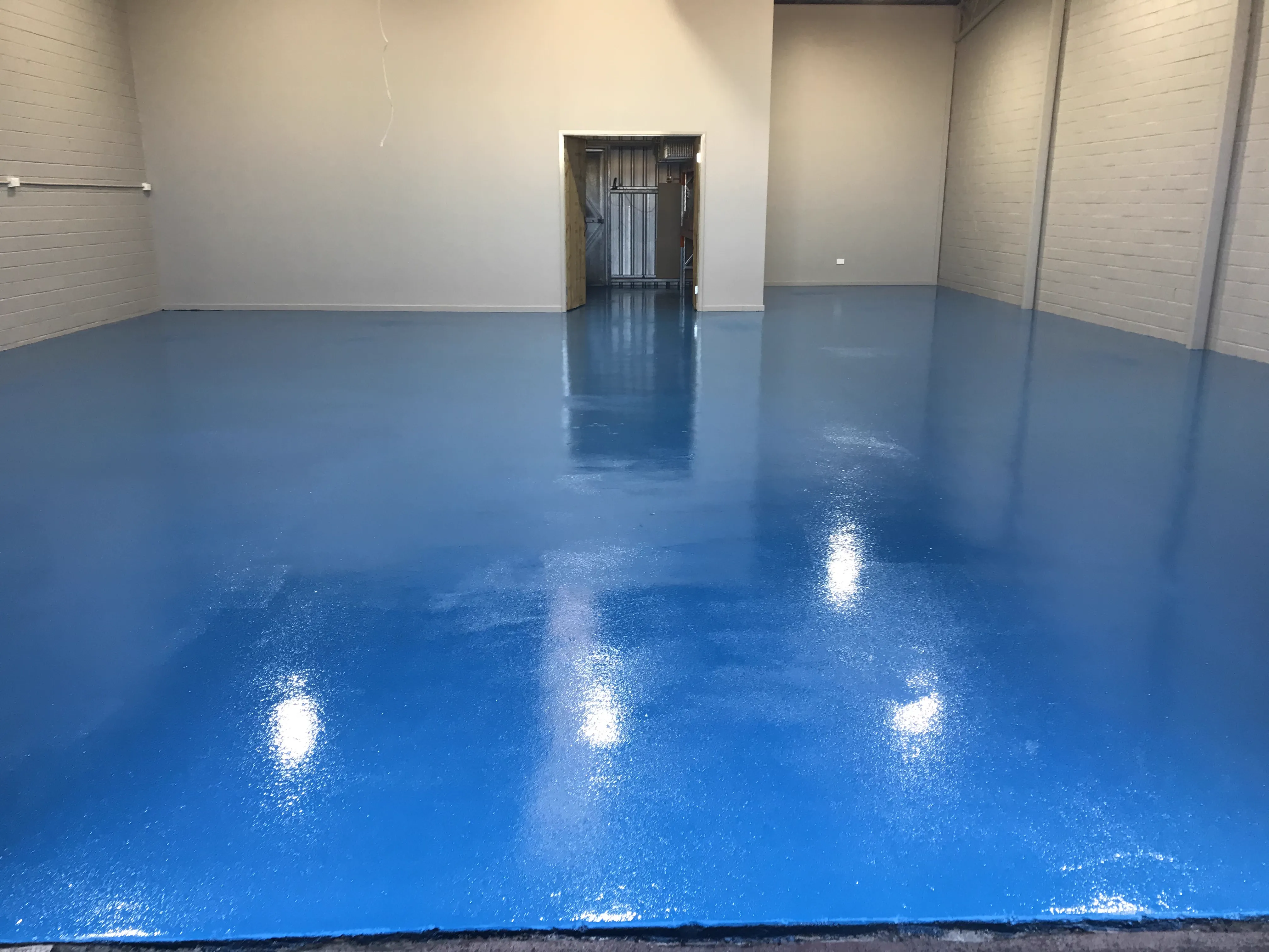 The same workshop floor after a solid blue plain epoxy coating with a high-gloss clear topcoat