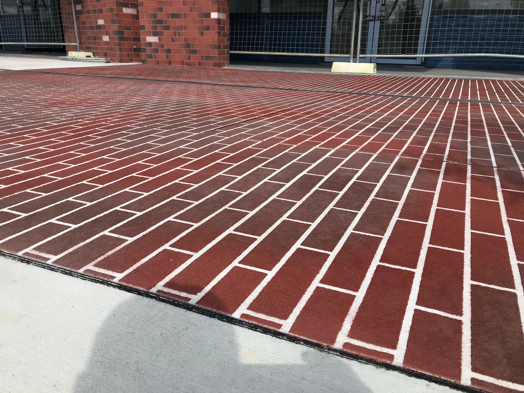 Deep red brick-pattern stencil concrete plaza with white joint lines beside a red brick pillar