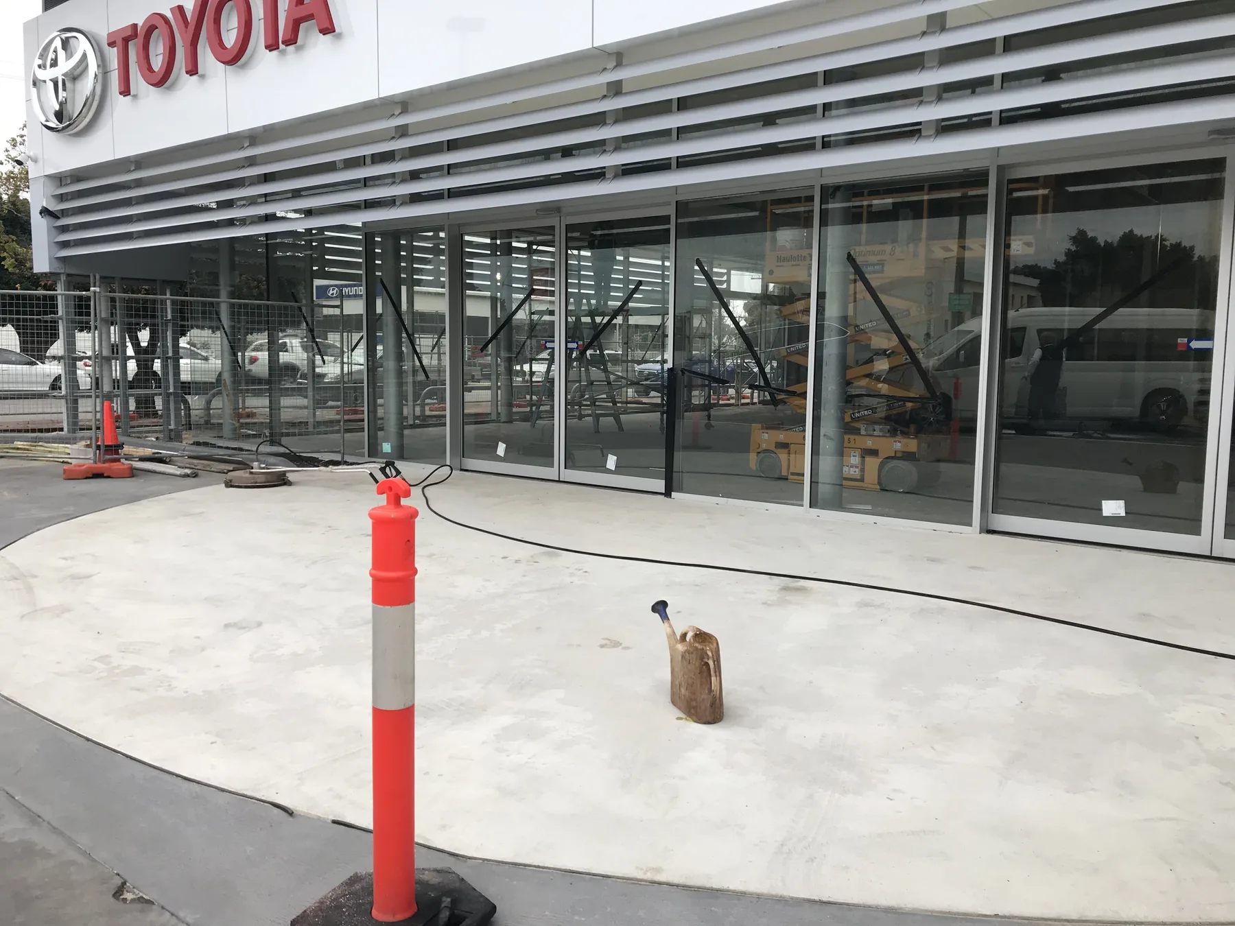Bare grey concrete forecourt at a Toyota dealership before stencil resurfacing, still fenced off