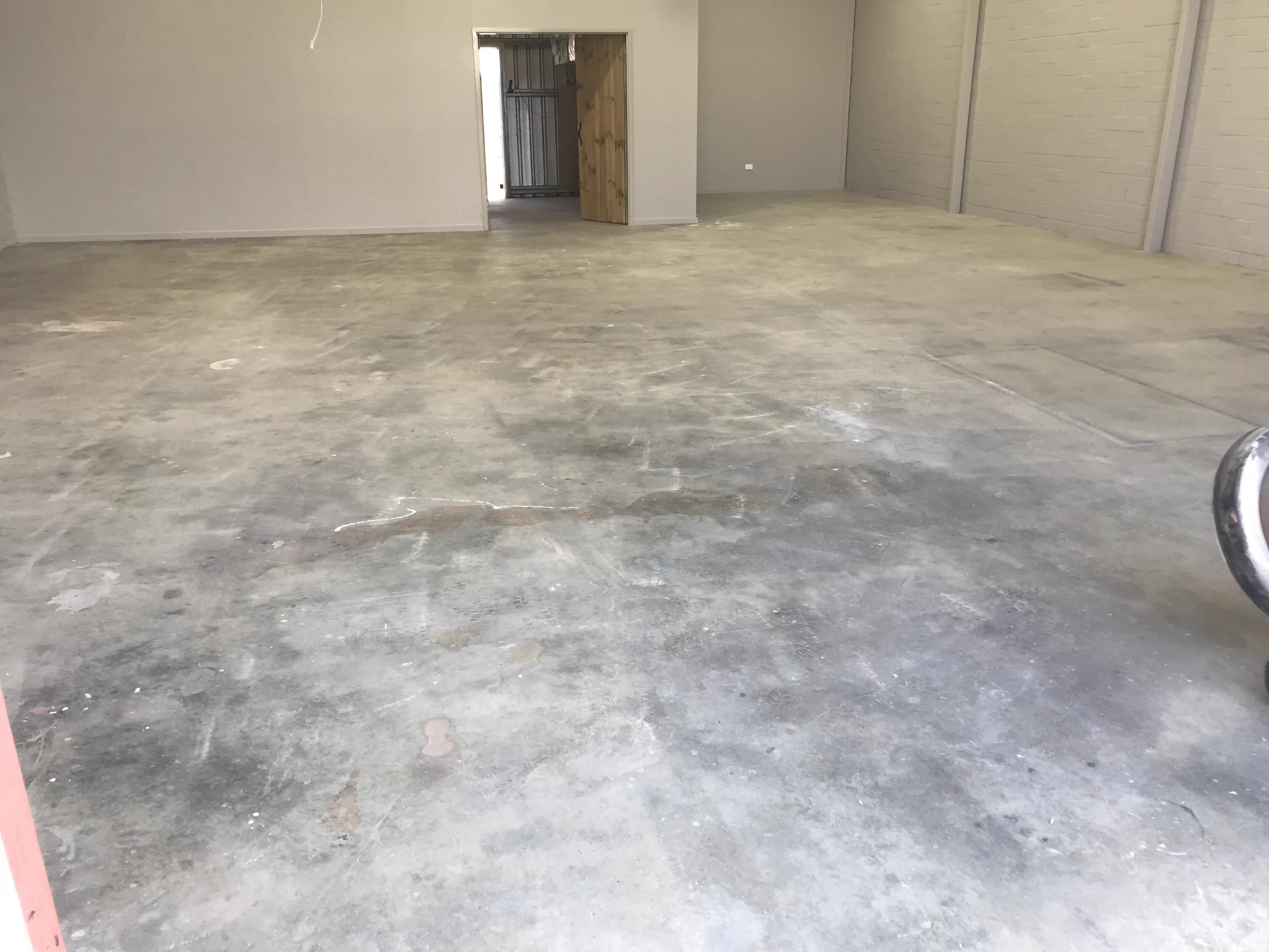 Bare concrete workshop floor before epoxy coating, showing stains, dust and unfinished surface