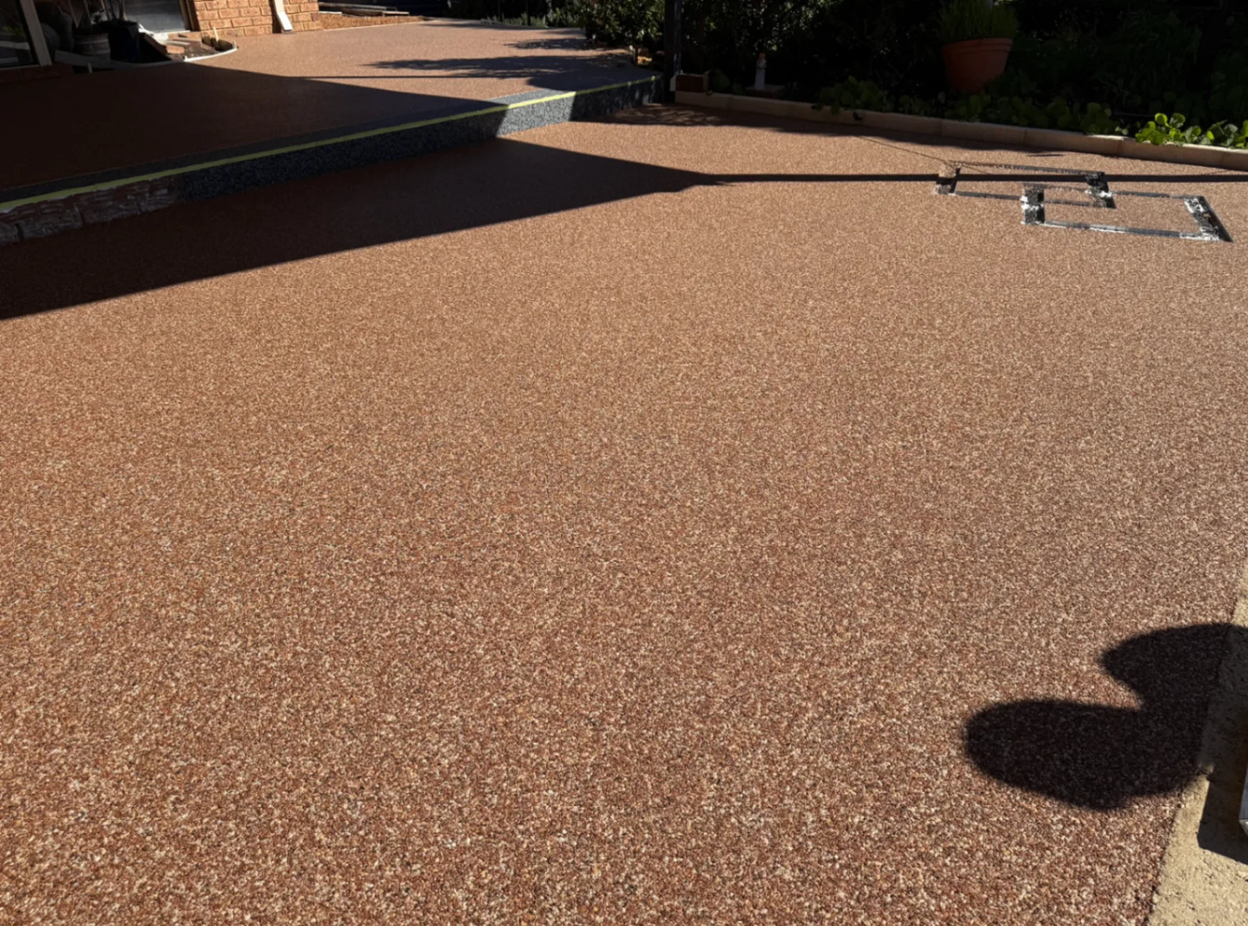 Completed terracotta-toned Vuba resin-bound driveway running past a charcoal exposed aggregate step in Perth