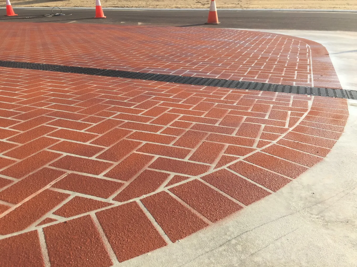 Terracotta herringbone spray-on paving with a curved border edge beside plain concrete