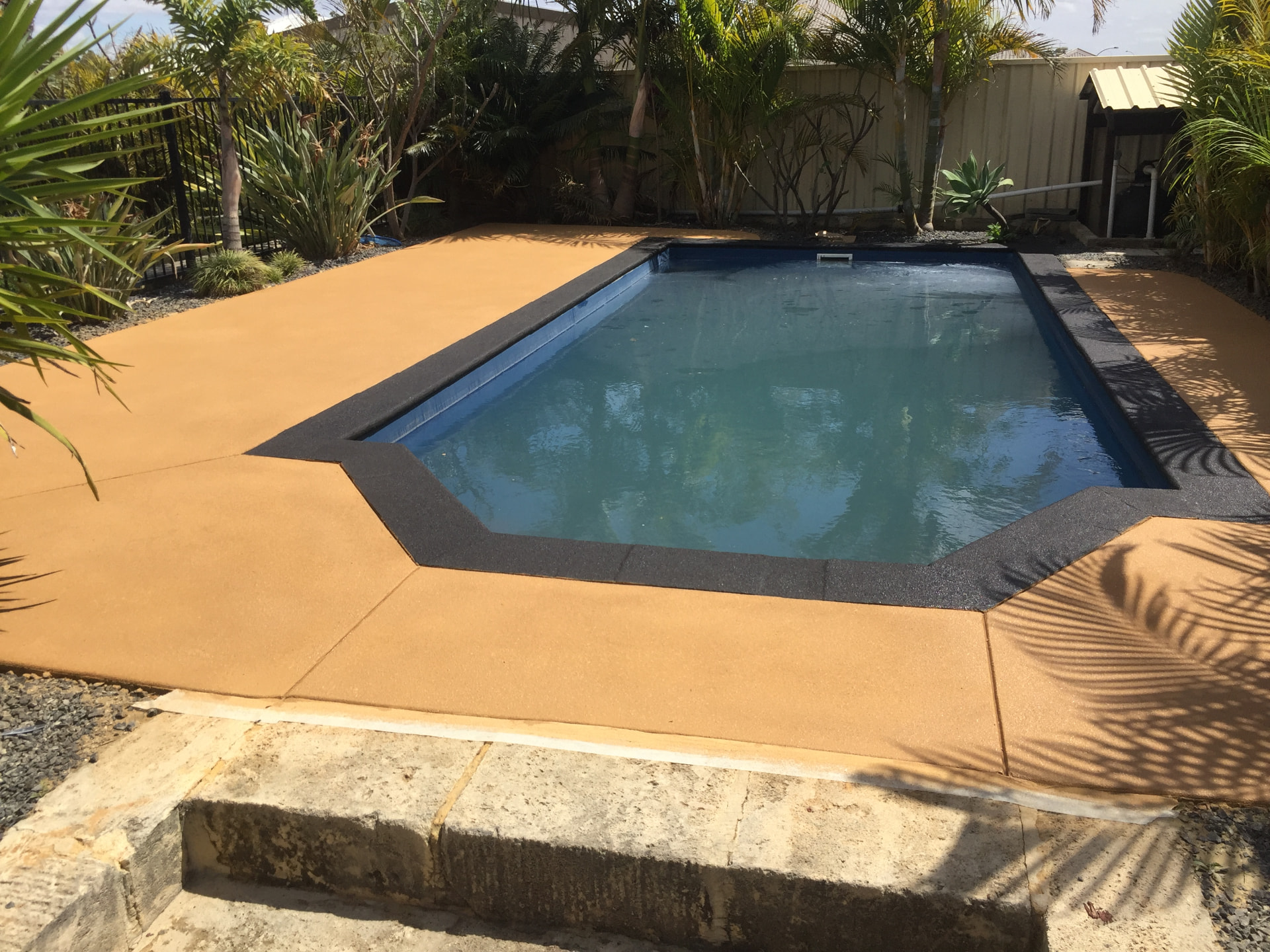 The same pool surround after spray-on concrete resurfacing in a warm sandstone colour with charcoal bullnose coping