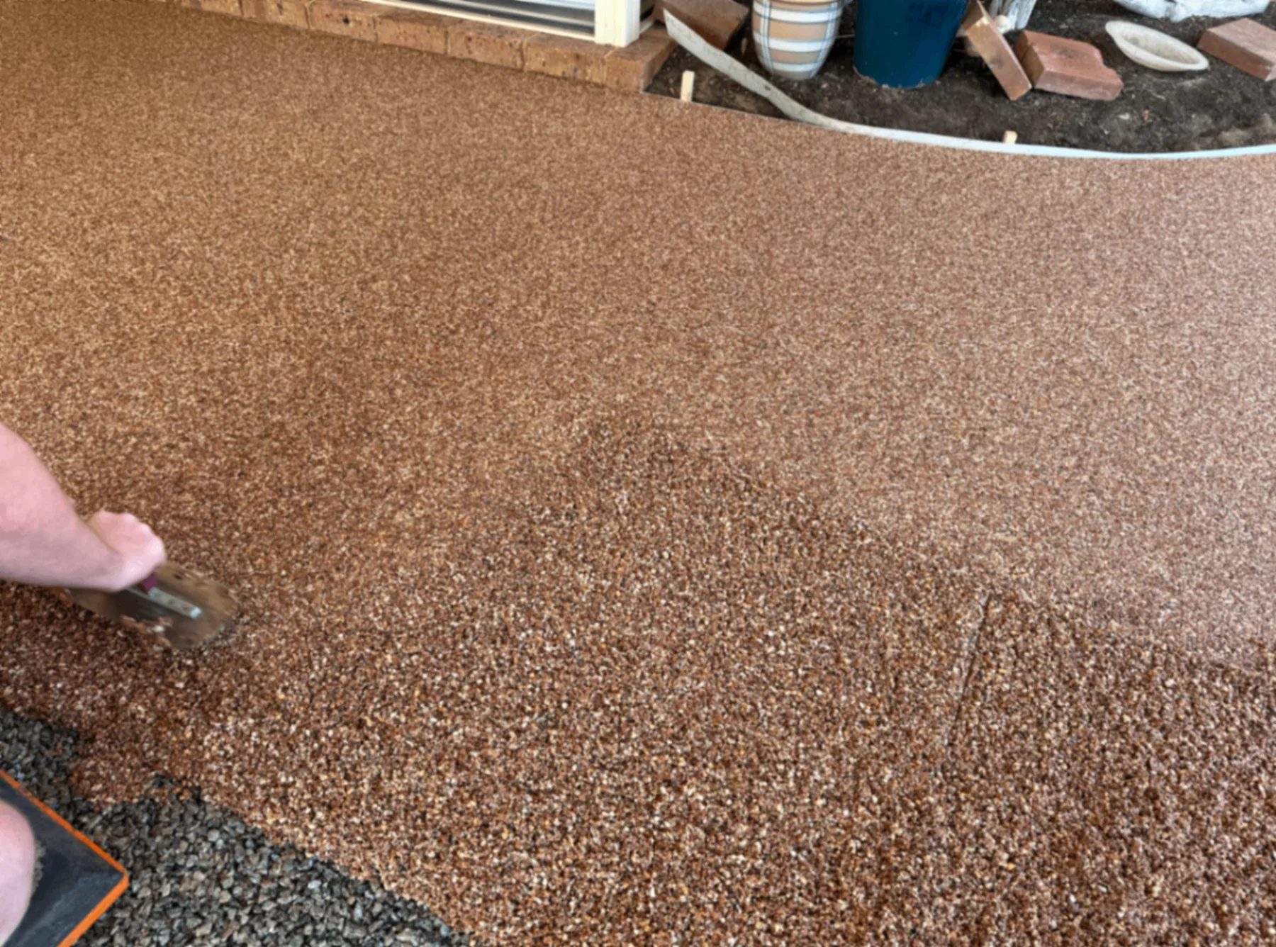 Close detail of copper Vuba resin-bound stone being smoothed with a hand trowel along a garden edge