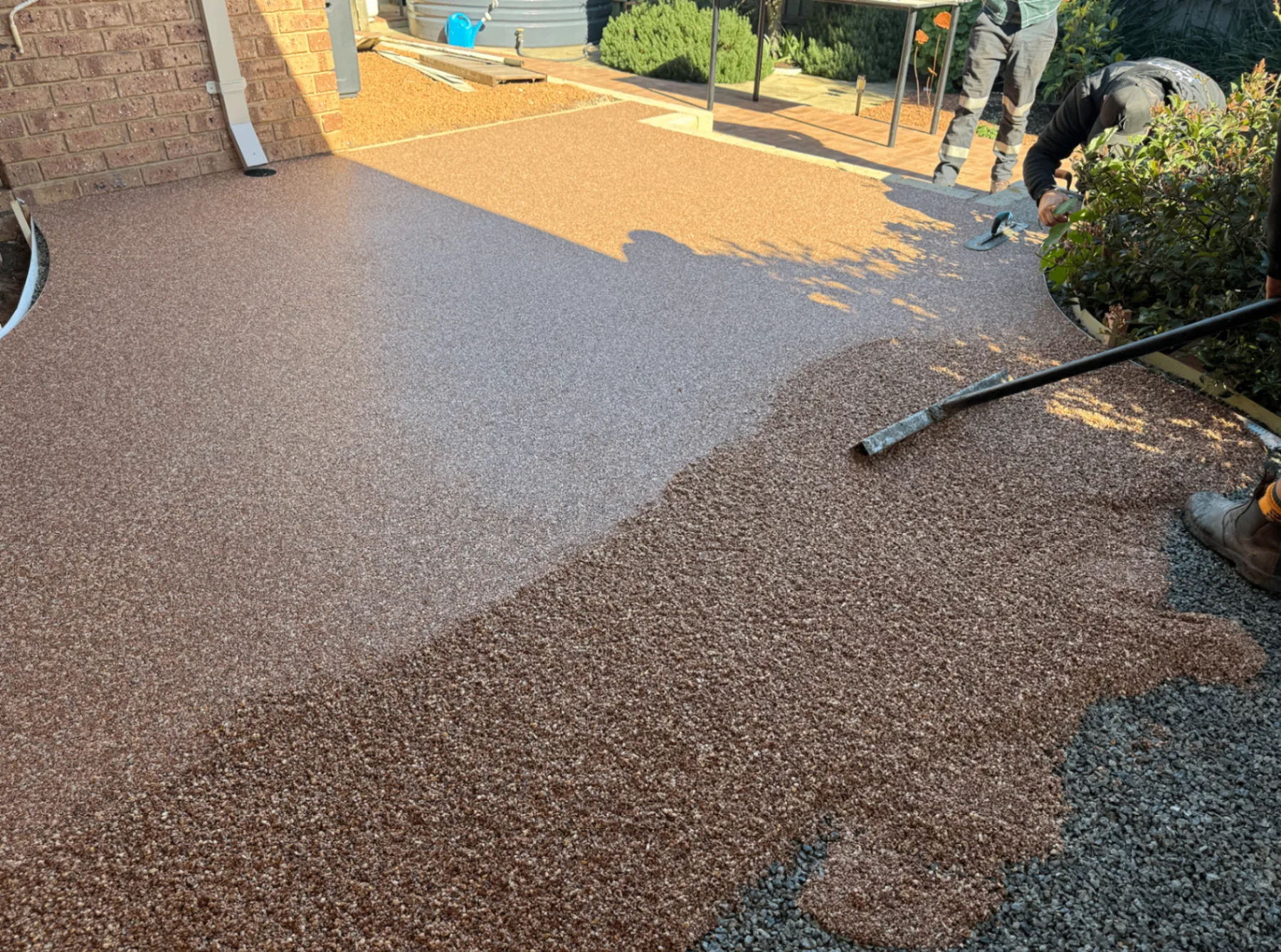 Copper resin-bound stone being trowelled level across a Perth courtyard beside loose aggregate