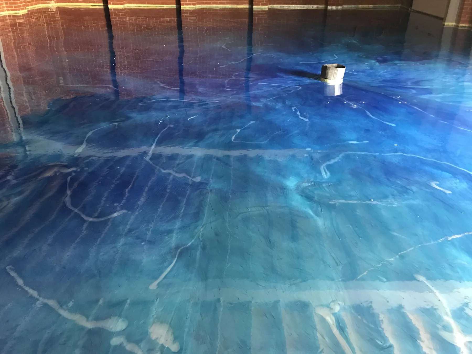 Blue metallic epoxy floor with deep marbled movement, reflecting the brick wall above it