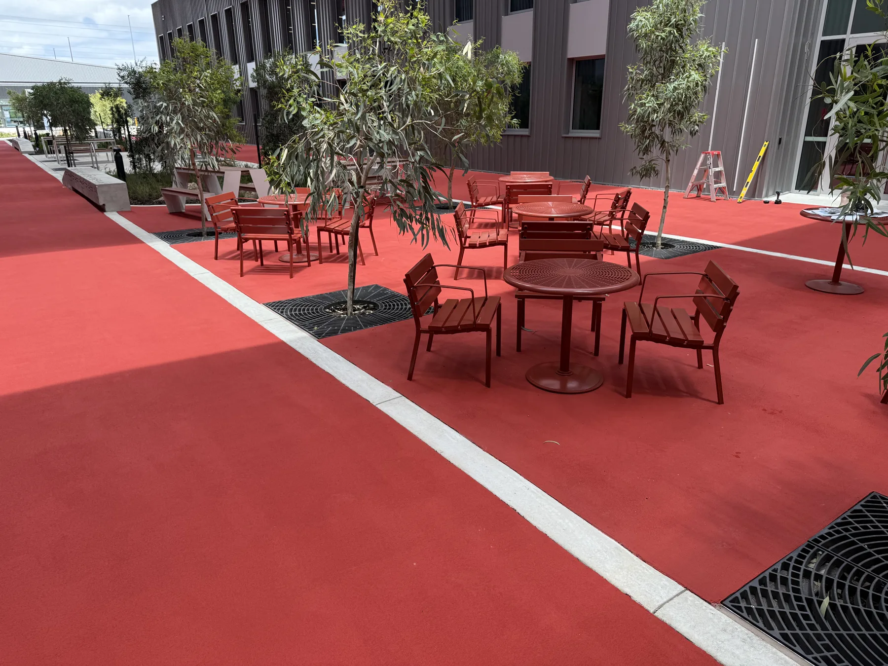 Red StreetBond plaza surface with red outdoor tables, chairs and planted trees at a commercial campus