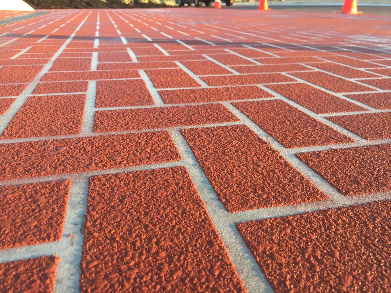 Red brick-pattern spray-on paving laid over a concrete driveway, photographed low to the surface